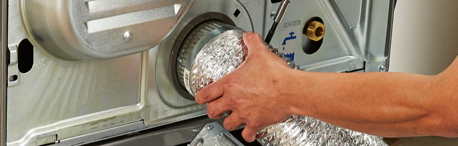 A person attaches the vent hose to a dryer.