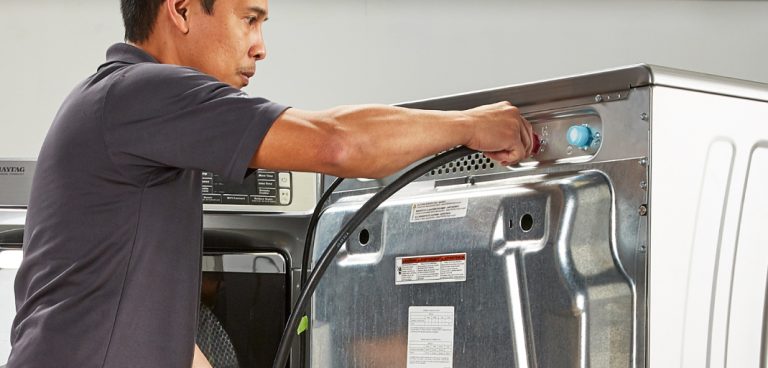 Une personne débranche le cordon derrière une laveuse lors du désinstallage de l’appareil.