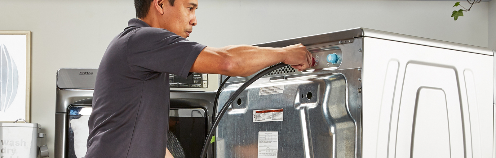A person removing the cord behind a washing machine while uninstalling the appliance.