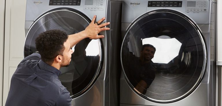 Un technicien déplace un appareil de lessive pour le placer à côté d’un autre. Une deuxième personne se tient à côté de lui.