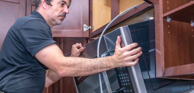 Un professionnel retire un four à micro-ondes avec hotte intégrée entre deux armoires.