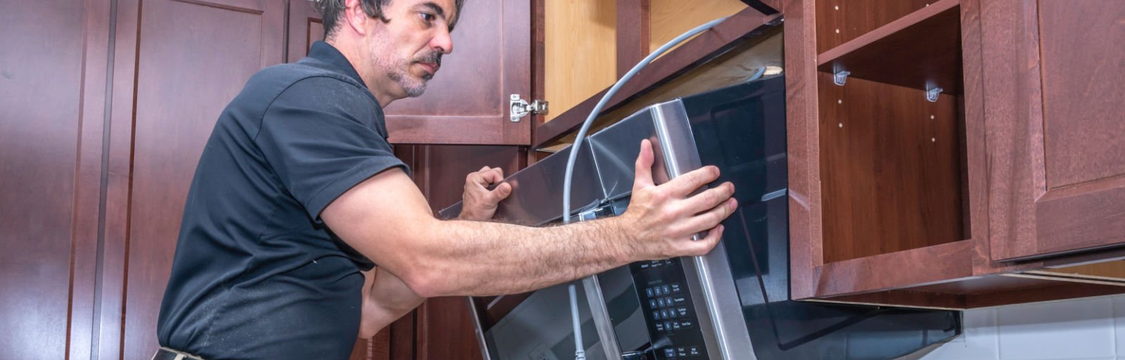 A professional removes an over-the-range microwave between cabinets.