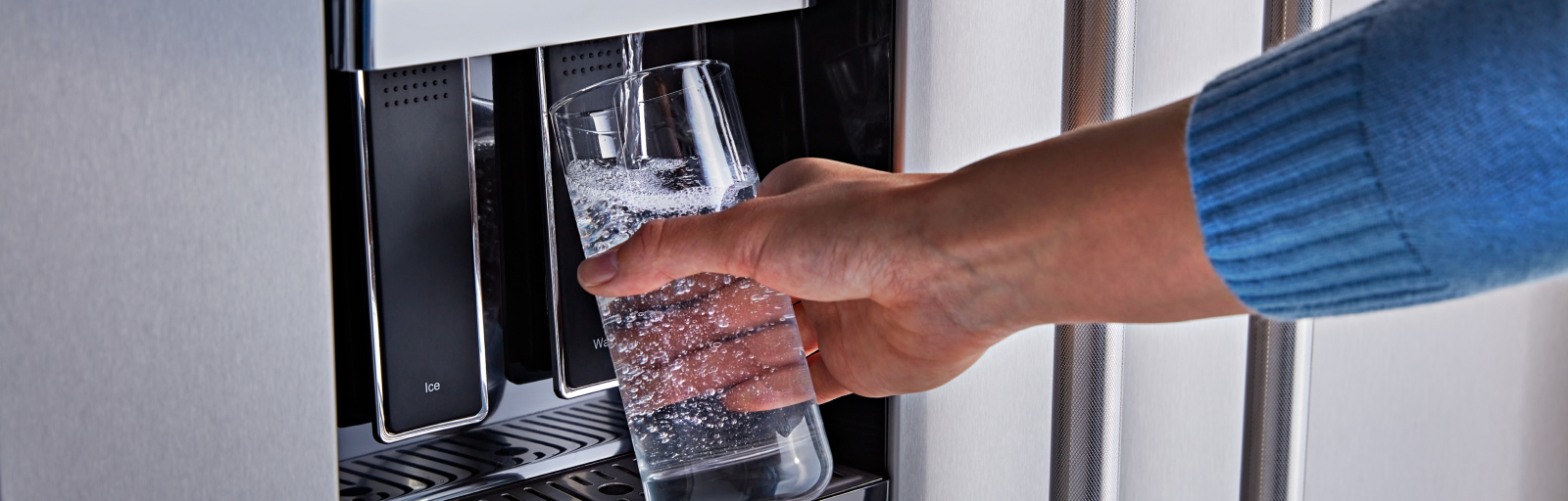 A person fills a glass with water from a fridge’s external water dispenser.