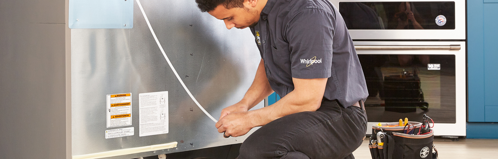 A professional installs a fridge. His tool belt is next to him.