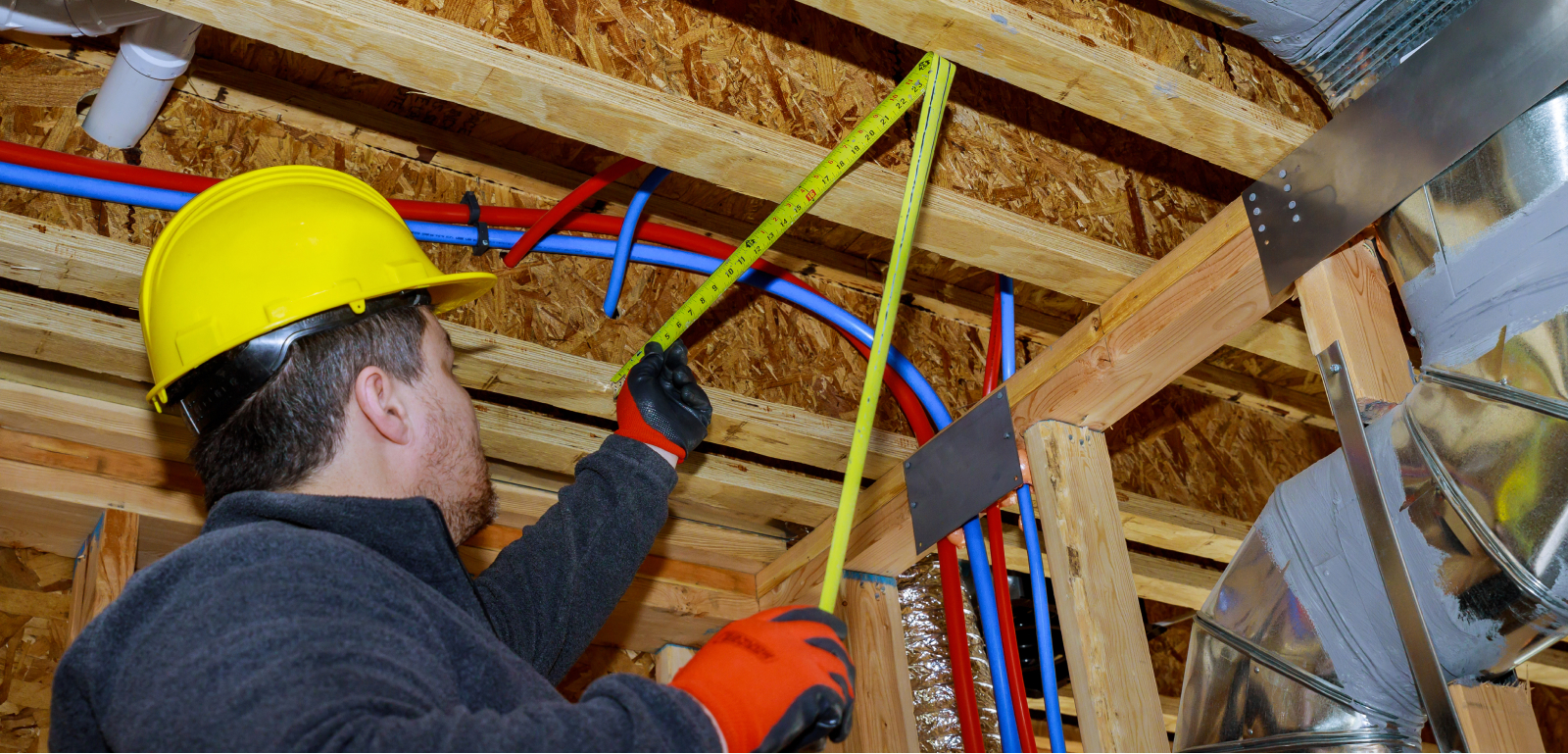 A man in a hard hat measures height with a tape measure.