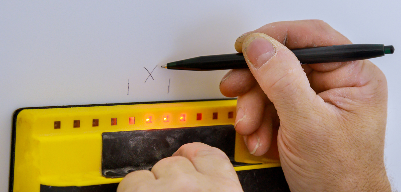 Someone marks a spot on a wall with a level and a pen.