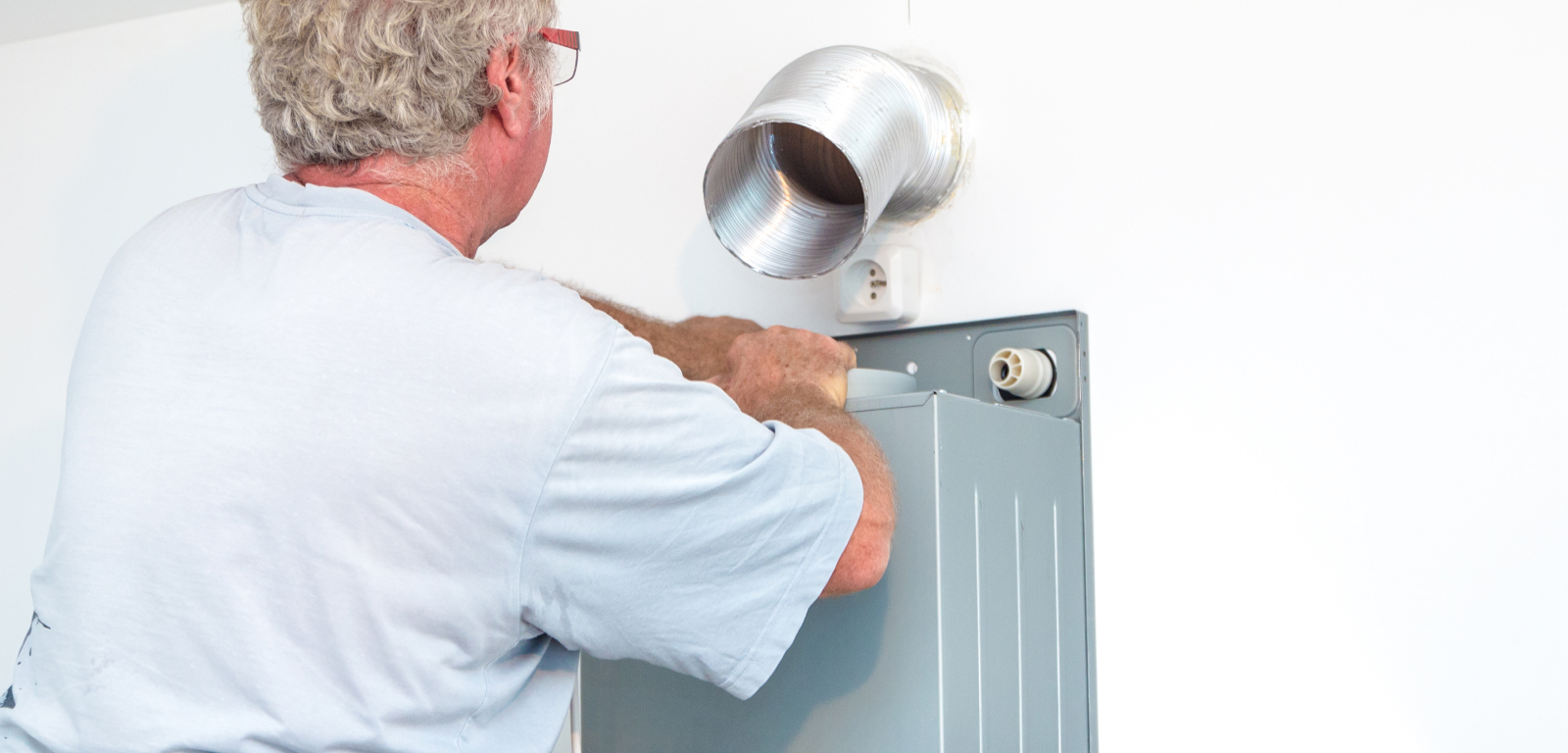 A man works on the kitchen vent that's outside the house.
