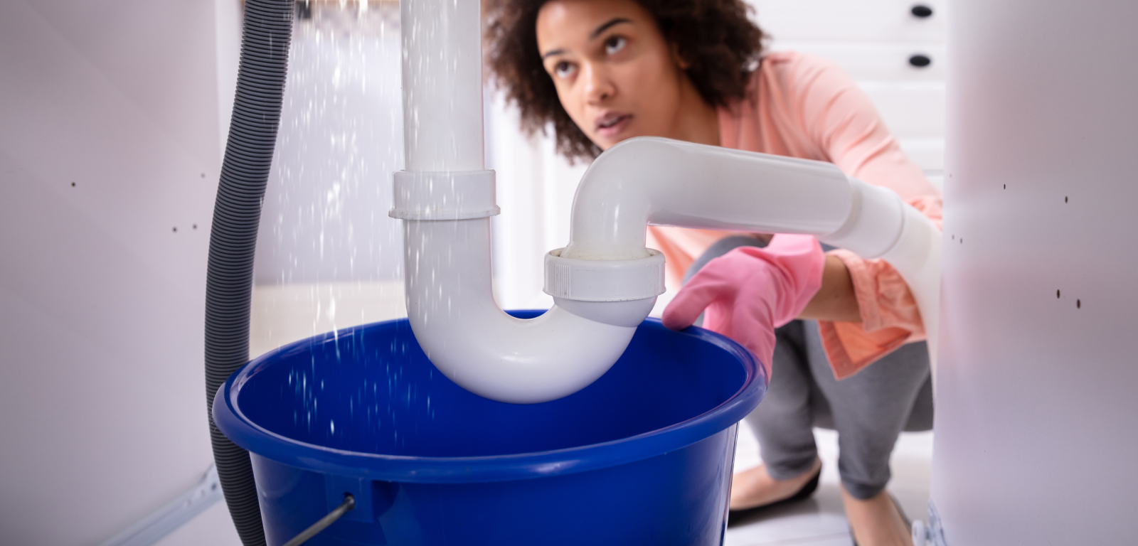 A person watching as water flows from the connection point into a bucket below.