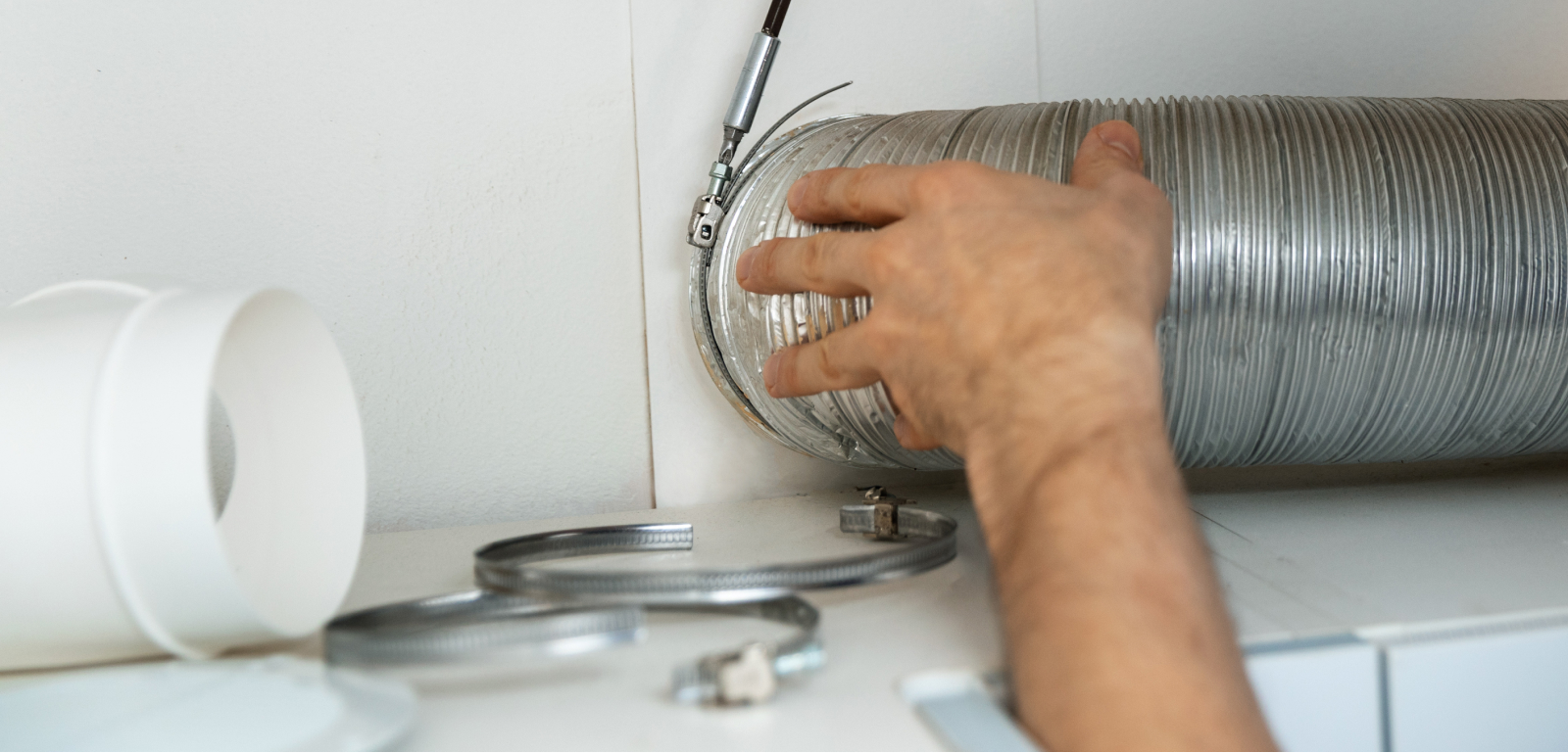 A hand touches the vent hose of a dryer.