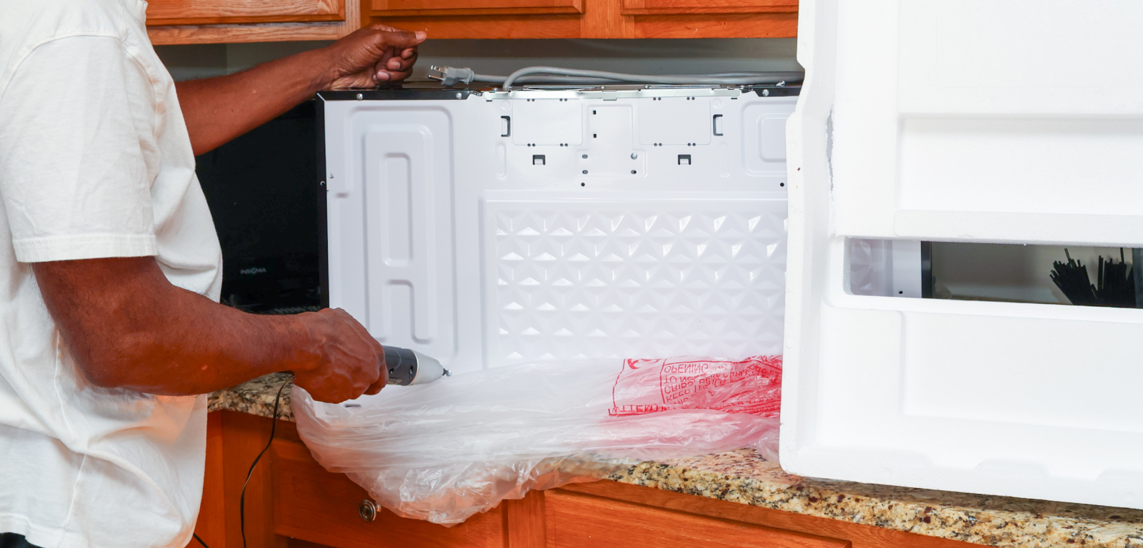 An installer uses an electric screwdriver on an over-the-range microwave in a kitchen.