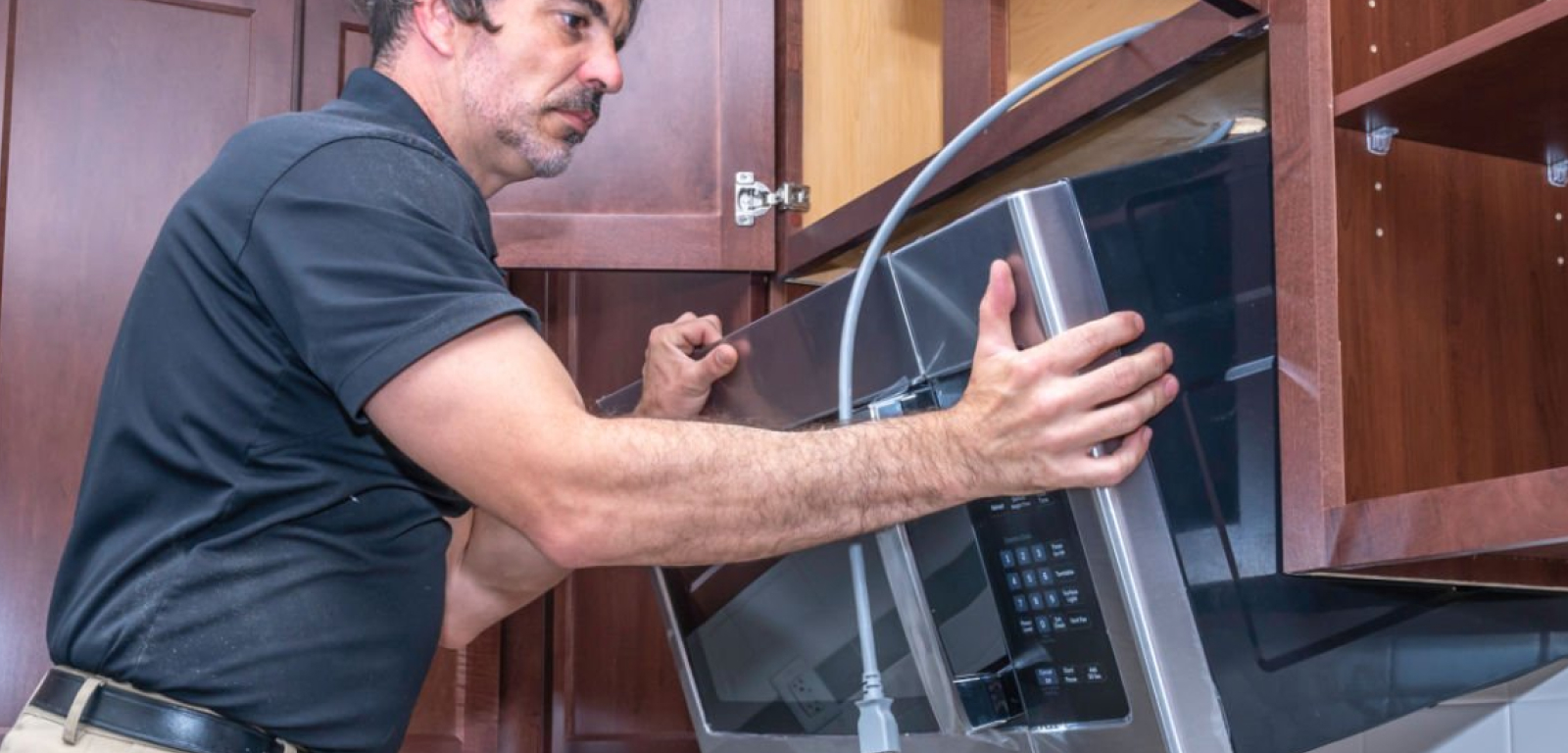 A professional removes an over-the-range microwave between cabinets.