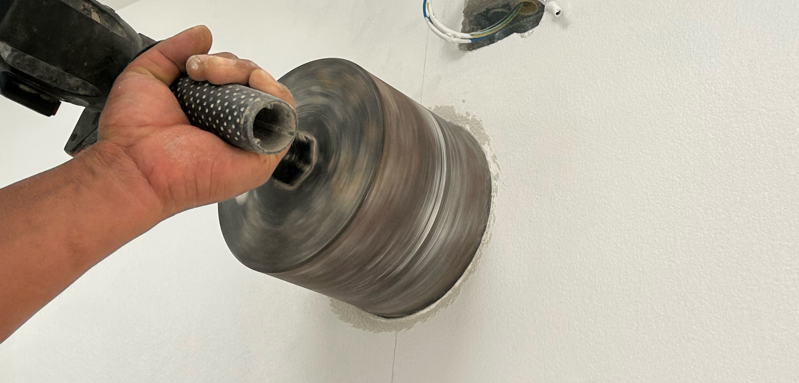 Someone drills into the exterior of a house with a large drill.