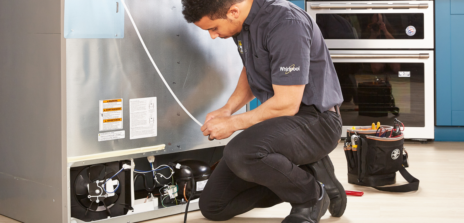 A professional installs a fridge. His tool belt is next to him.