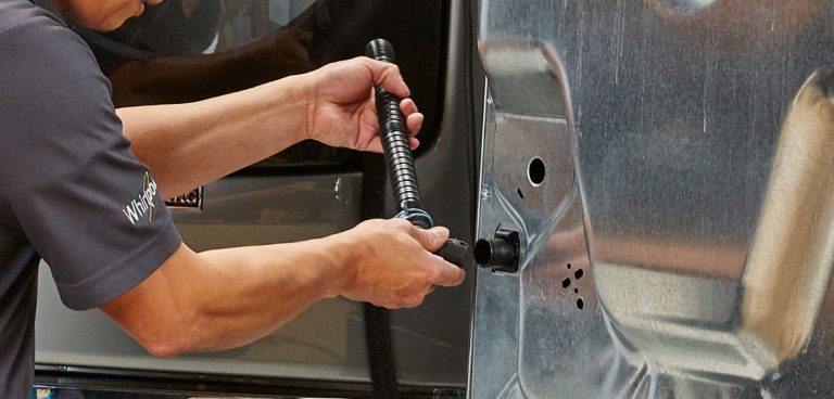 Une personne installe un tuyau de vidange sur une laveuse.