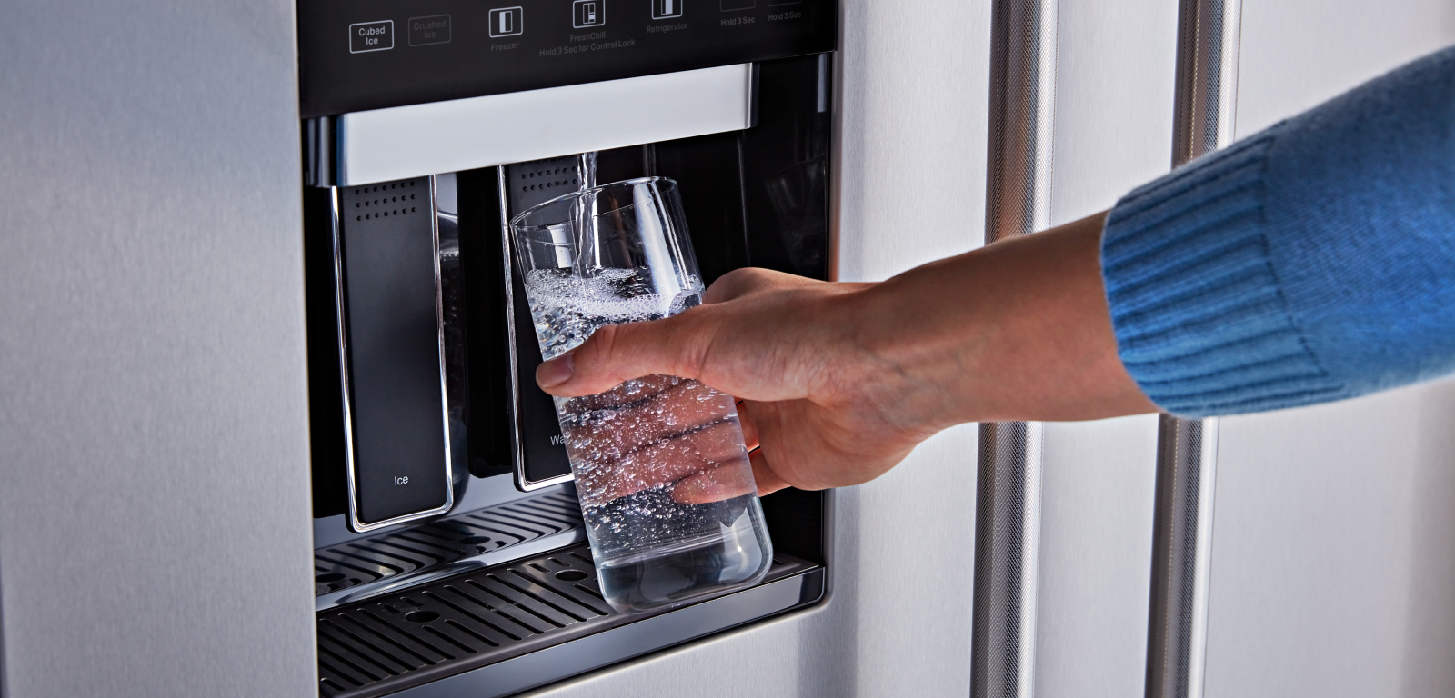 A person fills a glass with water from a fridge's external water dispenser.