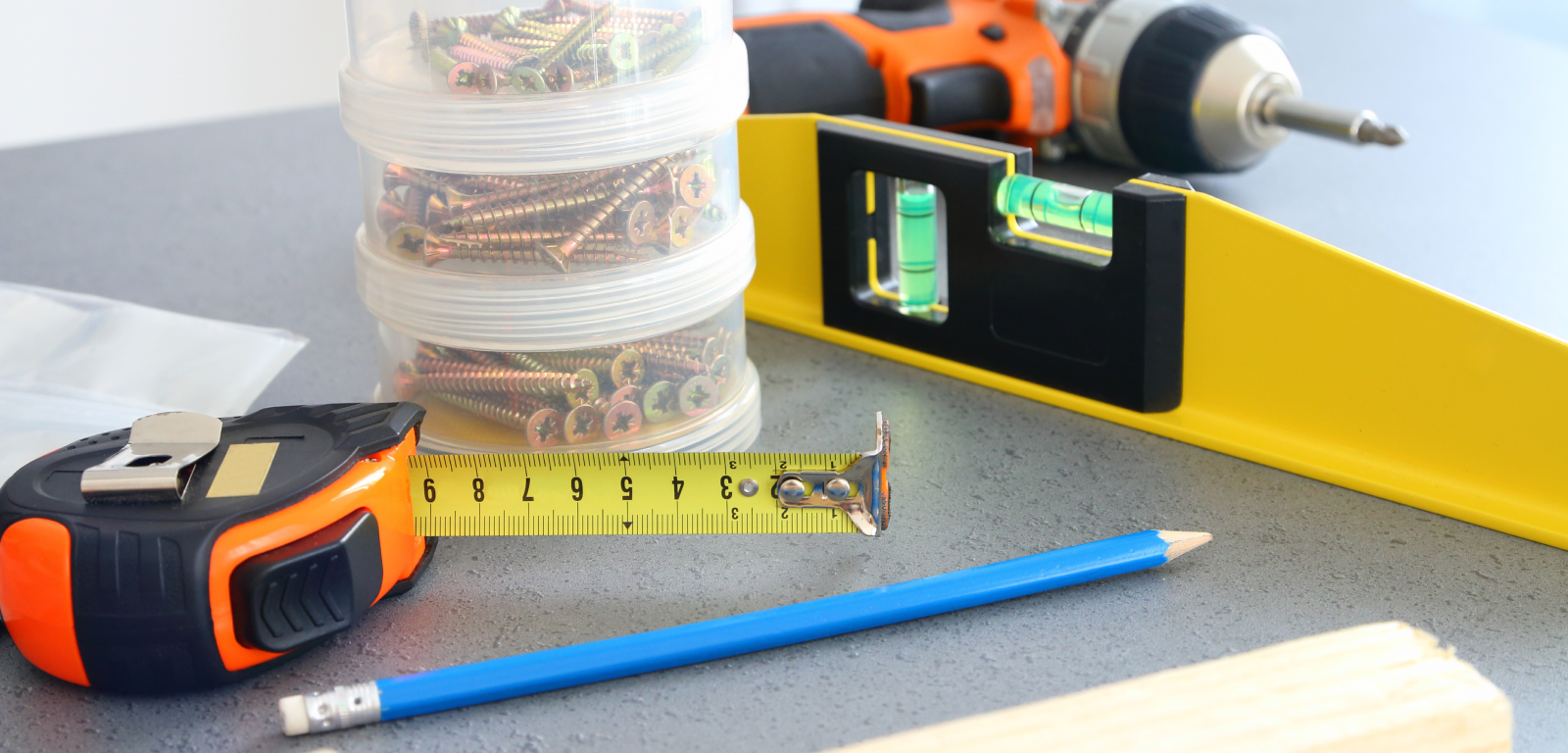 A tape measure, a stack of containers with screws, a pencil, a level, and a drill.