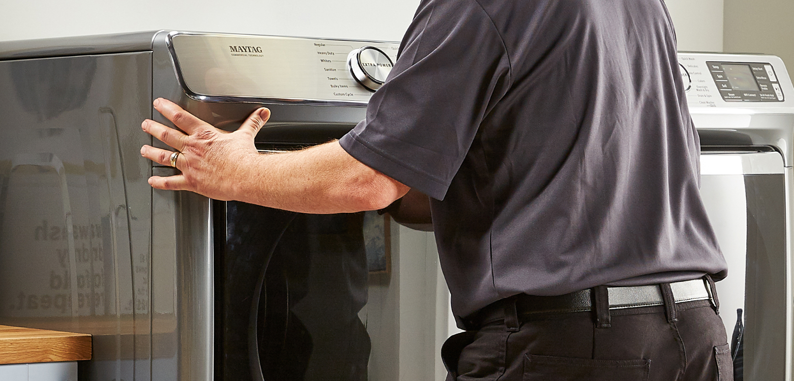 A person slides a laundry appliance away from the wall to uninstall it.