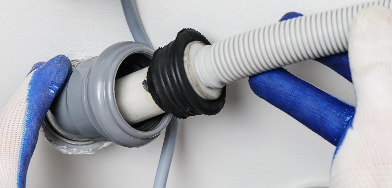 Gloved hands hold a pipe behind a laundry appliance.
