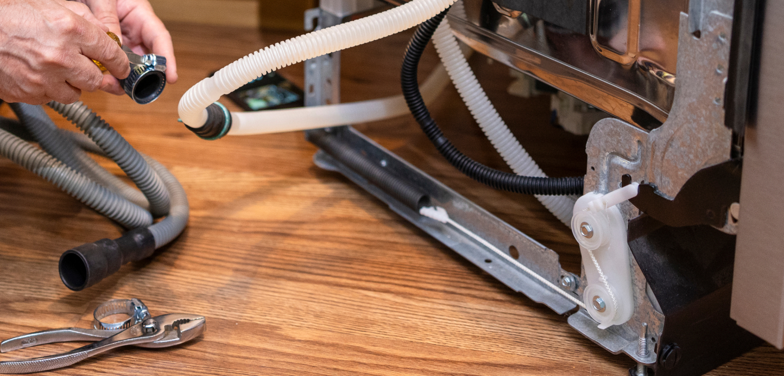 Img_Step7_1600x768 The back of a dishwasher with the hose visible. A person holds a small pipe.